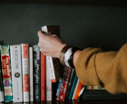 person picking white and red book on bookshelf