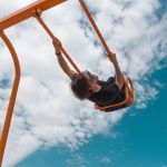 girl in black shirt and blue denim jeans riding on orange swing under blue and white