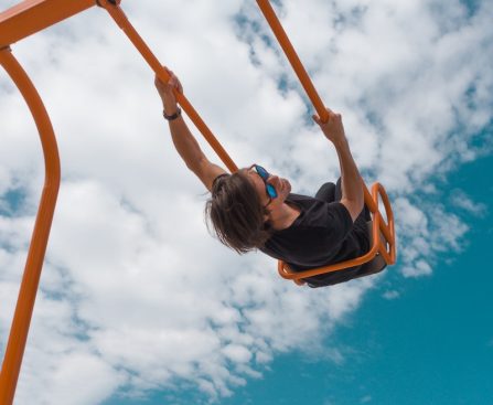 girl in black shirt and blue denim jeans riding on orange swing under blue and white